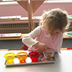 Little girl playing on the table with beads in a cup